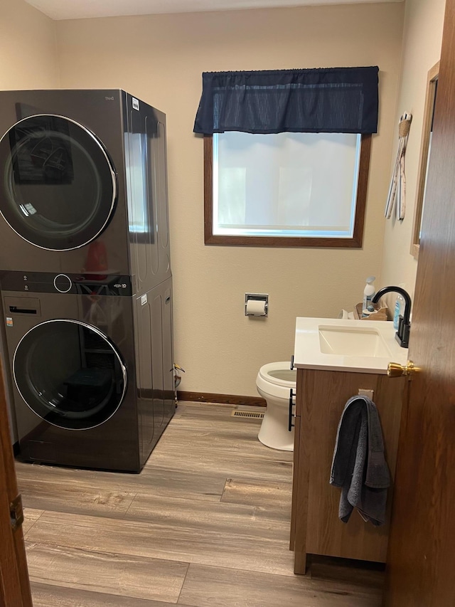 bathroom with stacked washer / dryer, baseboards, toilet, wood finished floors, and vanity