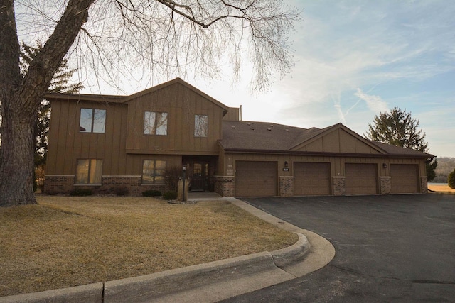 view of front of home with a front lawn, aphalt driveway, board and batten siding, a garage, and brick siding