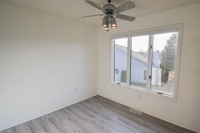 unfurnished room featuring wood finished floors, a healthy amount of sunlight, visible vents, and ceiling fan