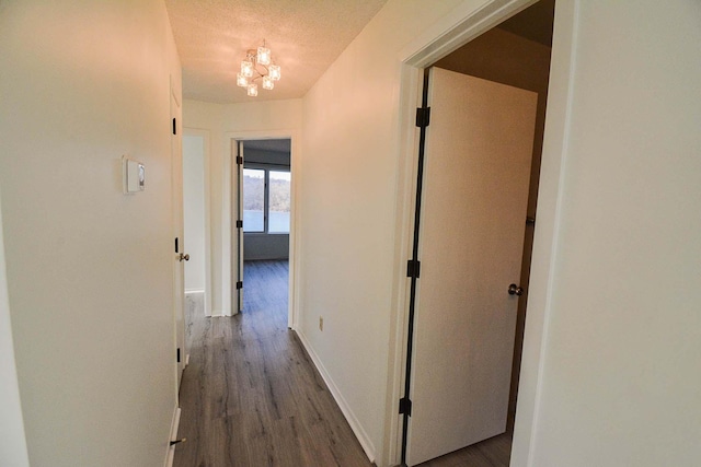 corridor with a notable chandelier, wood finished floors, baseboards, and a textured ceiling