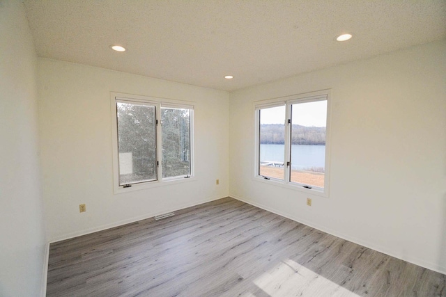 spare room with recessed lighting, plenty of natural light, wood finished floors, and a water view