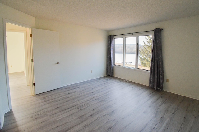 unfurnished room featuring a textured ceiling, a water view, and wood finished floors