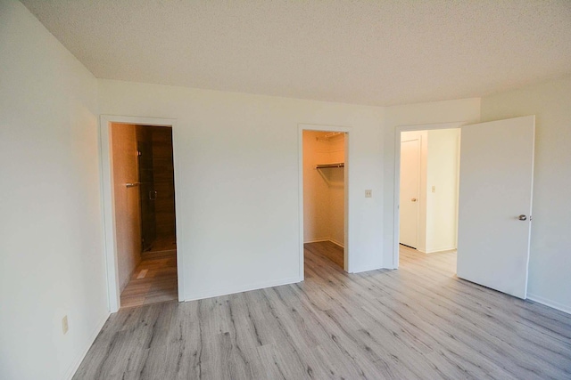 unfurnished bedroom with a spacious closet, a closet, ensuite bathroom, a textured ceiling, and light wood-type flooring