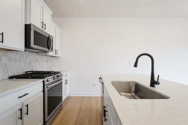 kitchen featuring light wood finished floors, a sink, stainless steel appliances, light countertops, and backsplash