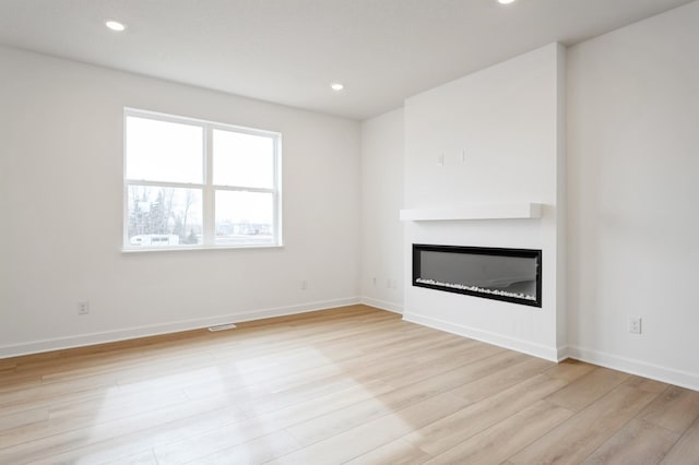 unfurnished living room with a glass covered fireplace, recessed lighting, baseboards, and light wood finished floors