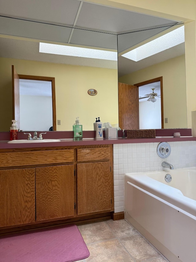 full bathroom featuring tile patterned floors, a garden tub, a ceiling fan, a skylight, and vanity