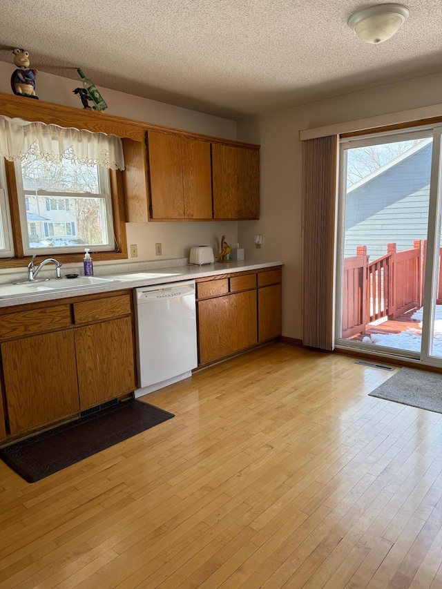 kitchen featuring a sink, brown cabinetry, white dishwasher, and light countertops