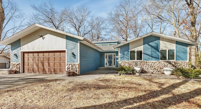 mid-century home featuring concrete driveway, a garage, and stone siding