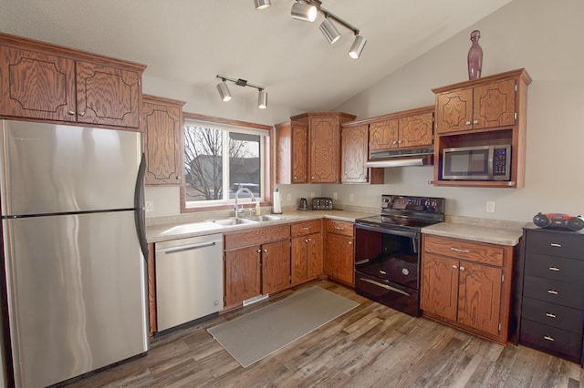 kitchen with a sink, stainless steel appliances, vaulted ceiling, light countertops, and under cabinet range hood