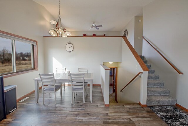 dining area featuring stairway, wood finished floors, baseboards, high vaulted ceiling, and an inviting chandelier