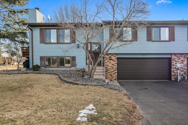 raised ranch with a front yard, driveway, a chimney, a garage, and brick siding