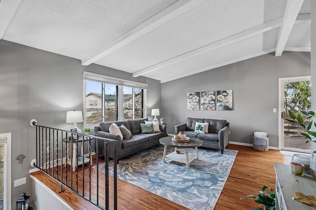 living area featuring a textured ceiling, vaulted ceiling with beams, baseboards, and wood finished floors