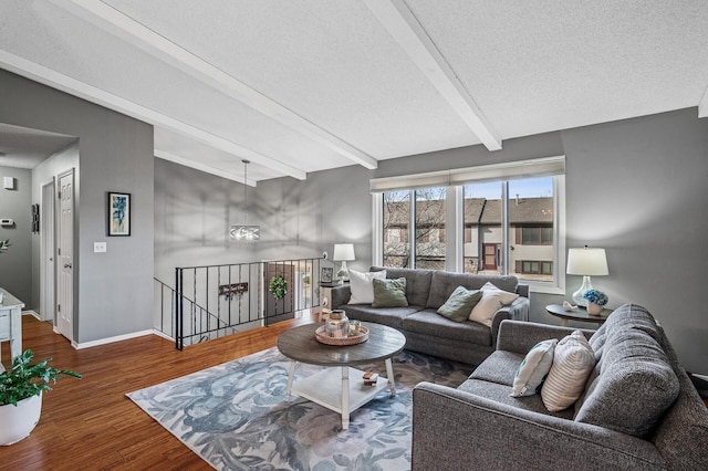 living area featuring beam ceiling, a textured ceiling, baseboards, and wood finished floors