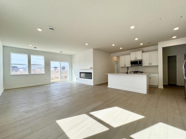 kitchen featuring stainless steel microwave, light wood-style floors, open floor plan, and decorative backsplash