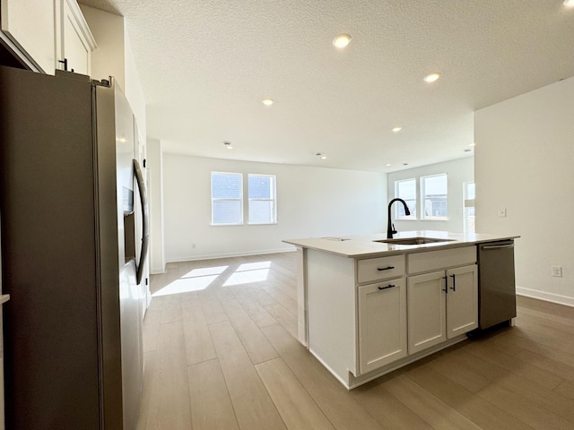 kitchen with light wood-style flooring, a sink, stainless steel appliances, white cabinetry, and open floor plan