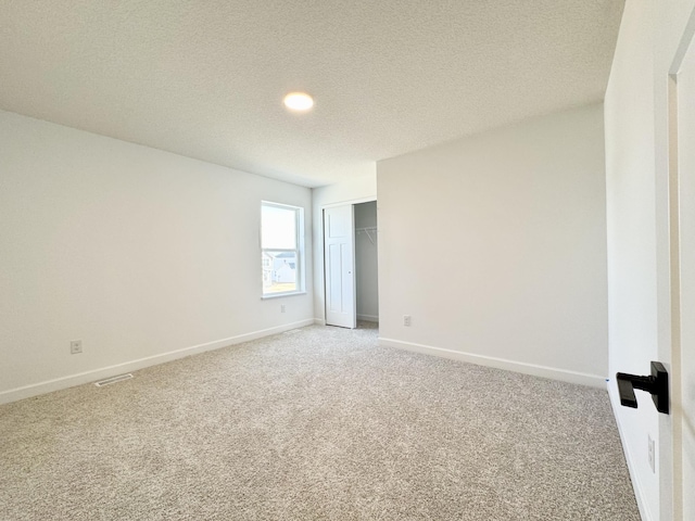 spare room featuring baseboards, light carpet, a textured ceiling, and visible vents