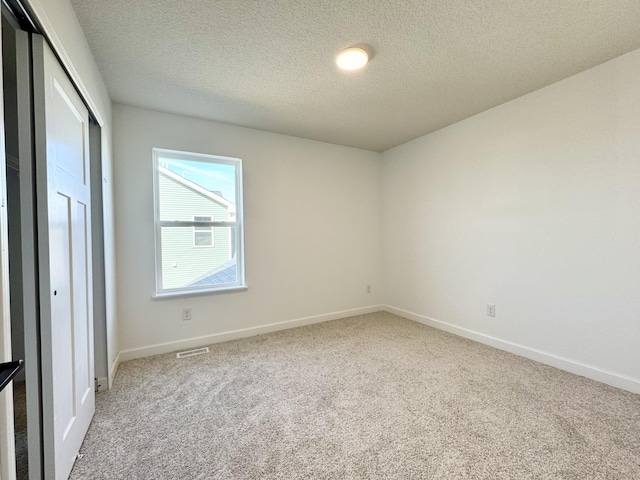 empty room featuring visible vents, light colored carpet, a textured ceiling, and baseboards