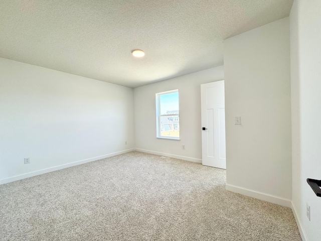 unfurnished room with light colored carpet, baseboards, and a textured ceiling