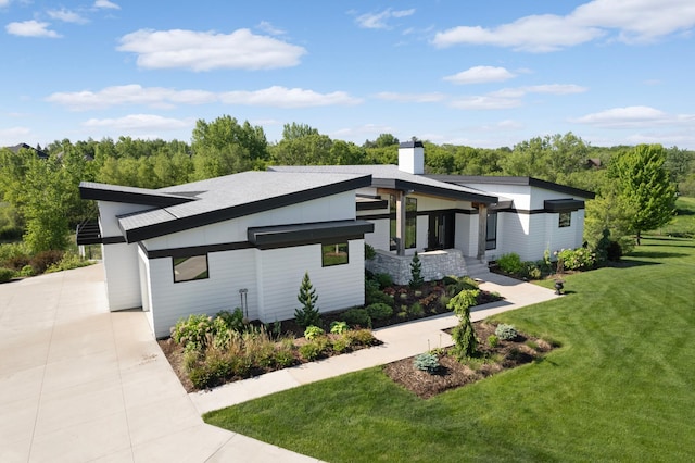 modern home featuring a front lawn, a chimney, and driveway