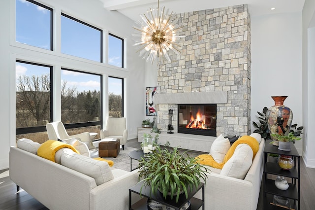 living area featuring wood finished floors, baseboards, a stone fireplace, a towering ceiling, and a chandelier