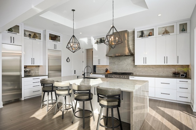 kitchen featuring a sink, a raised ceiling, wall chimney range hood, and stainless steel built in fridge