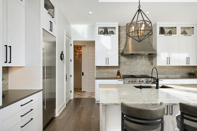 kitchen with stainless steel built in refrigerator, a sink, decorative light fixtures, tasteful backsplash, and dark wood finished floors