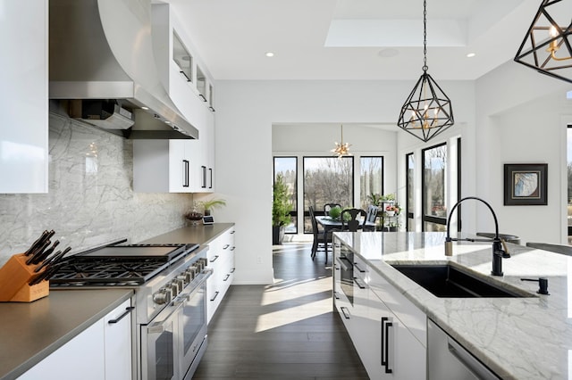 kitchen featuring a sink, appliances with stainless steel finishes, wall chimney exhaust hood, dark wood-style flooring, and hanging light fixtures