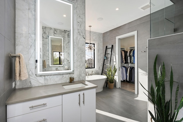 full bath featuring vanity, visible vents, a freestanding bath, a spacious closet, and tile walls