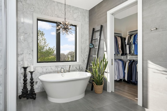 full bathroom with a freestanding tub, a notable chandelier, tile walls, and a walk in closet