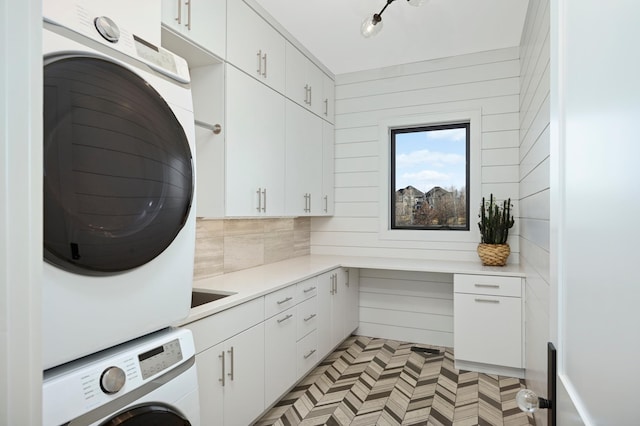 laundry area with cabinet space, wooden walls, and stacked washing maching and dryer