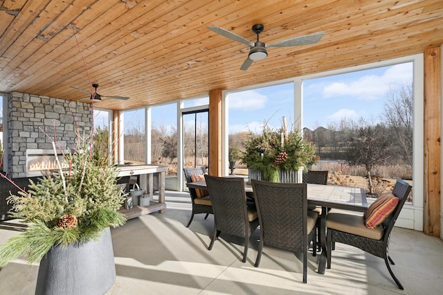 sunroom / solarium with a ceiling fan, wood ceiling, and an outdoor stone fireplace