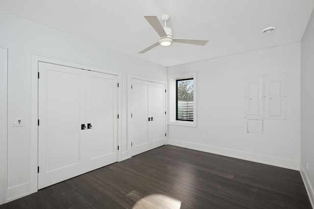 unfurnished bedroom featuring baseboards, multiple closets, dark wood-style floors, and a ceiling fan