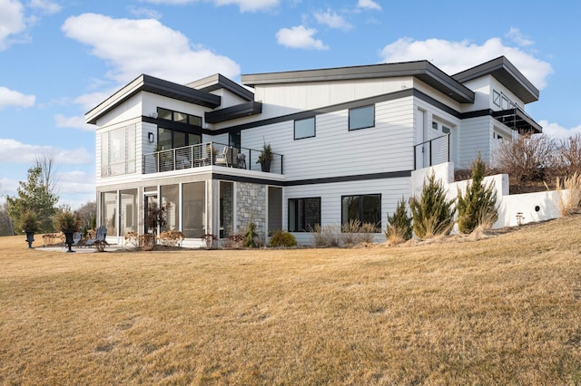 rear view of property with a patio area, a balcony, a lawn, and stone siding