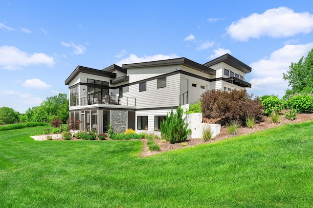 rear view of property featuring a yard, a garage, a balcony, and stone siding