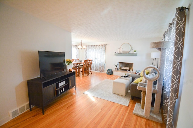 living room with visible vents, a textured ceiling, wood finished floors, baseboards, and a chandelier