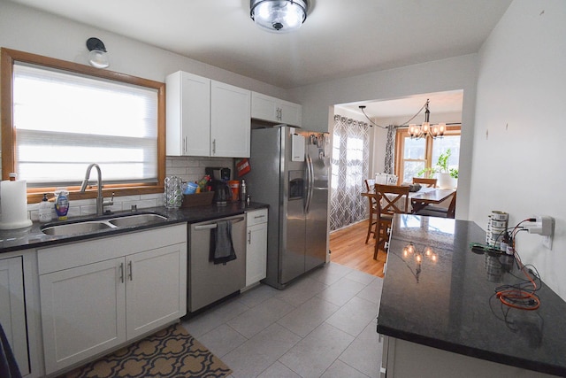 kitchen with tasteful backsplash, appliances with stainless steel finishes, a notable chandelier, white cabinets, and a sink