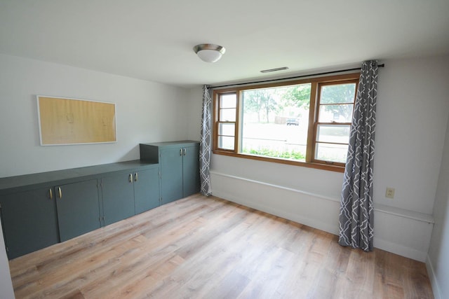 spare room featuring light wood finished floors, visible vents, and baseboards