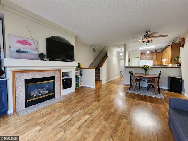 living room with baseboards, stairway, light wood-style flooring, a fireplace, and a textured ceiling