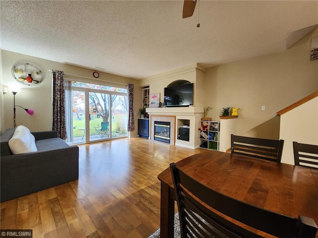 living room with a fireplace, a textured ceiling, a ceiling fan, and wood finished floors