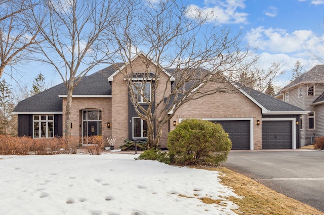 traditional home with a garage, brick siding, roof with shingles, and aphalt driveway