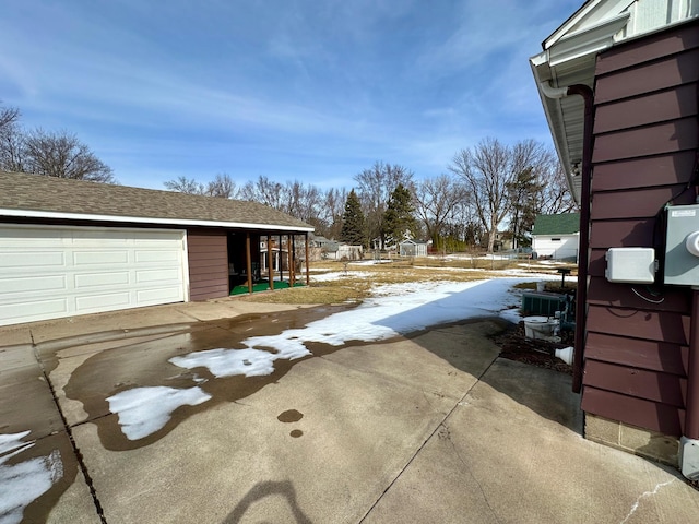 snow covered property with a garage, an outbuilding, and a shingled roof