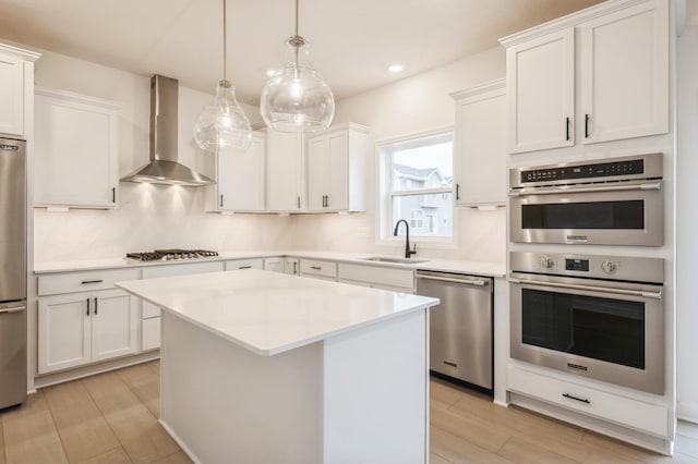 kitchen with a sink, stainless steel appliances, white cabinetry, and wall chimney range hood