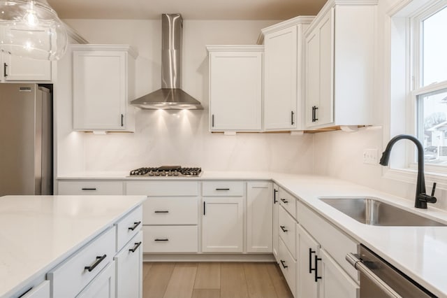 kitchen featuring a sink, white cabinetry, appliances with stainless steel finishes, wall chimney exhaust hood, and light countertops