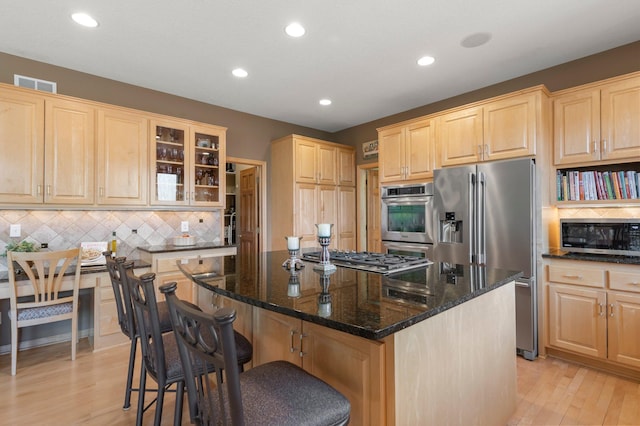 kitchen featuring visible vents, light brown cabinetry, dark stone counters, light wood-type flooring, and appliances with stainless steel finishes