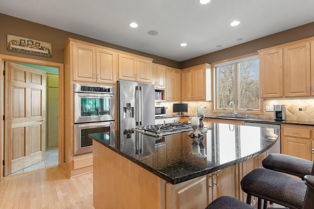 kitchen featuring light brown cabinetry, backsplash, appliances with stainless steel finishes, and a kitchen breakfast bar