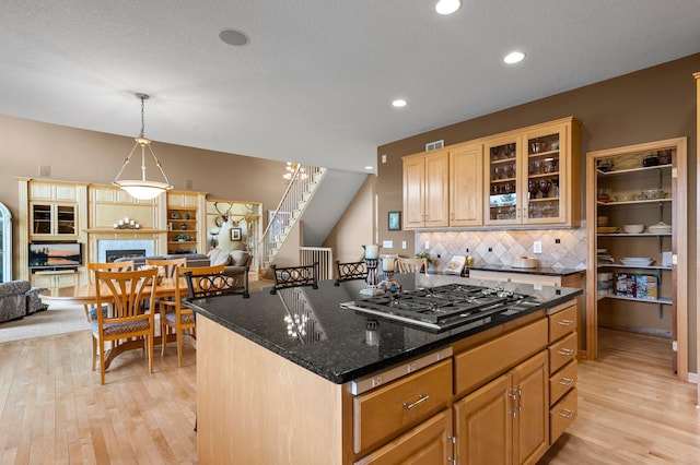 kitchen featuring glass insert cabinets, open floor plan, light wood-type flooring, decorative backsplash, and stainless steel gas stovetop