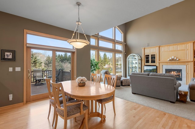 dining room featuring light wood finished floors, a fireplace, baseboards, and a towering ceiling