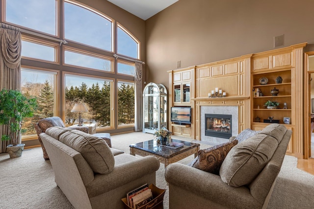 living area with a tiled fireplace, visible vents, light carpet, and a high ceiling