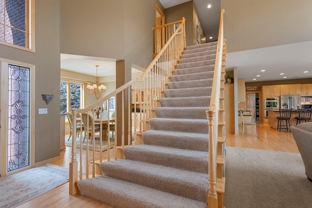 staircase with wood finished floors, baseboards, an inviting chandelier, recessed lighting, and a towering ceiling