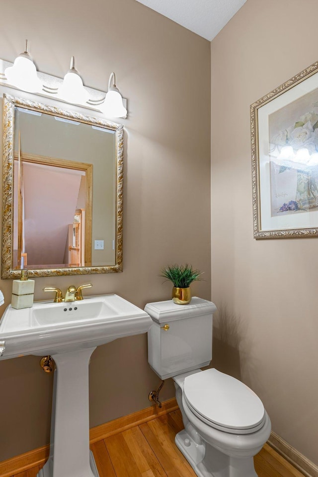 half bath featuring a sink, toilet, baseboards, and wood finished floors